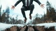 © Maximages  - A person in a business suit jumps over a cracked surface surrounded by a snowy environment with evergreen trees and distant mountains, showing strength and perseverance.