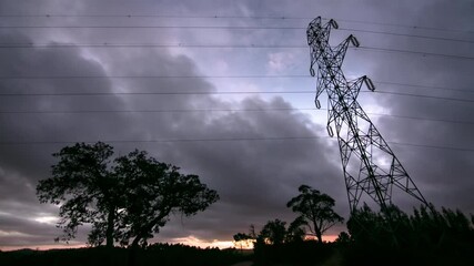 Wall Mural - Electricity lines and pylon silhouetted in front of moody timelapse sky