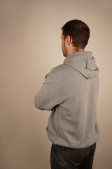 Back view. Handsome male. Neutral background. Man in casual clothes. Young guy standing in front of camera. Man looking at side. Crossed hands.