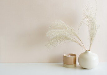 Canvas Print - Modern beige ceramic vase with dry fluffy flowers branch and candle on beige  wall background .Copy space, Aesthetic minimalist scandinavian interior accessories. 