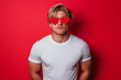 © ALL YOU NEED studio - handsome blonde man wearing mock-up blank white t-shirt , wearing heart-shaped red sunglasses on an isolated red background, a funny animal in the concept of love for Valentine's Day celebration