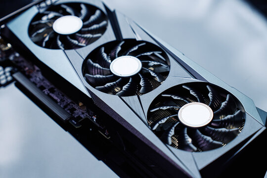 Close-up of high-performance graphics card with three cooling fans on dark background. Modern video card for gaming and advanced computing