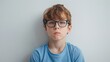 © vefimov - A young boy with glasses posing for a photograph indoors against a white wall.
