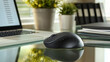 © Itsaraporn - Close-up of a wireless mouse beside a laptop on a glass desk, with office plants and files in the background