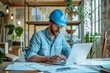 © Tetyana - A portrait of a male general contractor working at a computer in his office wearing a blue protective helmet
