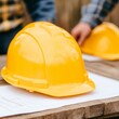 © MetaKibo - Yellow construction helmets on a wooden table with blueprints.
