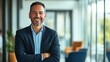 © Anton - Smiling businessman in office setting, arms crossed