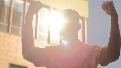 1Happy winner successful African American university student guy man male outdoors in city education success good results win achieve winning in sun sunshine rise hands champion victory achievement