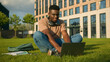 © Yuliia - Happy smiling African American man university college academy student guy teenager male studying homework online on grass meadow in park study learning with book copybook laptop prepare for exam study