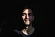 © SerPak - A young man stands confidently, illuminated by soft light that highlights his features against a contrasting dark background. The play of light creates a dramatic yet serene atmosphere, showcasing his