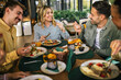 © Mediteraneo - Group of happy friends eating lunch together in a restaurant. They eat delicious salads, hamburgers, bread and meat.
