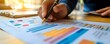 © Ytnart - A hand holding a pen points at various graphs and charts on a document, showcasing data analysis and business strategy.