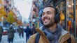 © COK House - A young man in a beard smiles with wireless headphones, walking in the city with a grey scarf and jacket, enjoying music in a cheerful urban scene.
