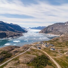 Canvas Print - Aerial view of a small village nestled between rocky hills and a fjord with icebergs.