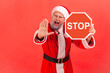 © khosrork - Portrait of excited angry elderly man with gray beard wearing santa claus costume showing red stop sign and ban with palm, screaming.