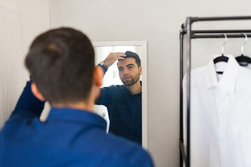 Attractive young man preening in front of the mirror in his home walk-in closet