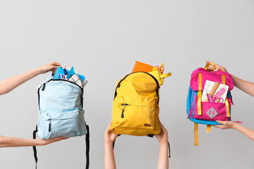 Wall Mural - Female hands with different backpacks and school supplies on grey background, closeup