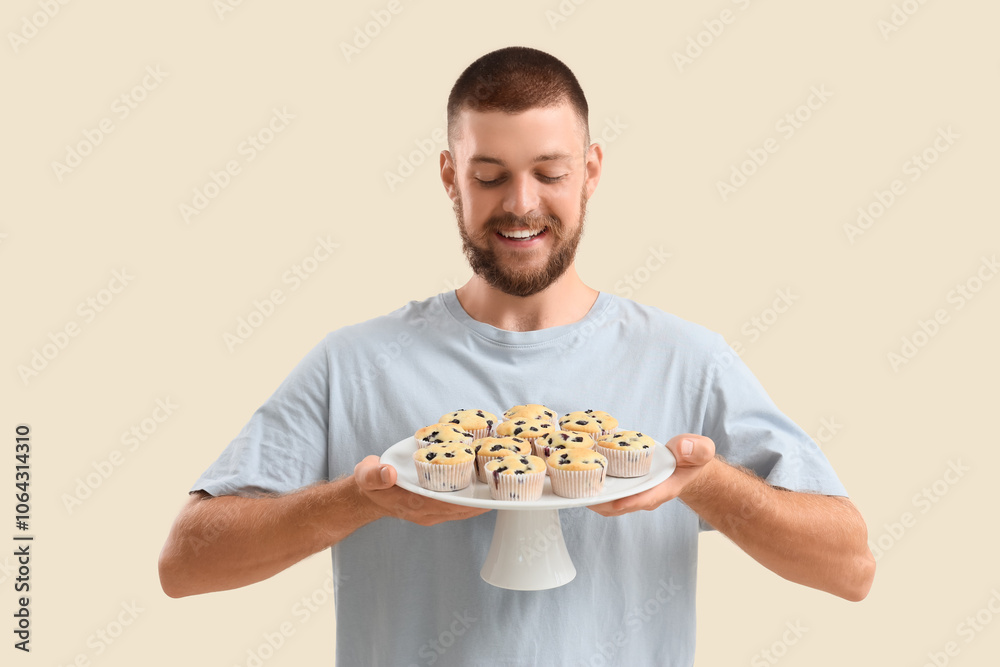 Young man with tasty muffins on beige background