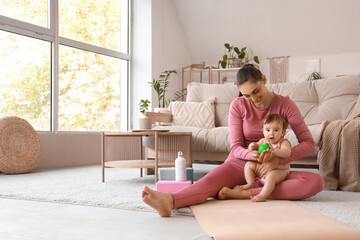 Sporty young mother with her little baby and massage ball sitting on mat at home