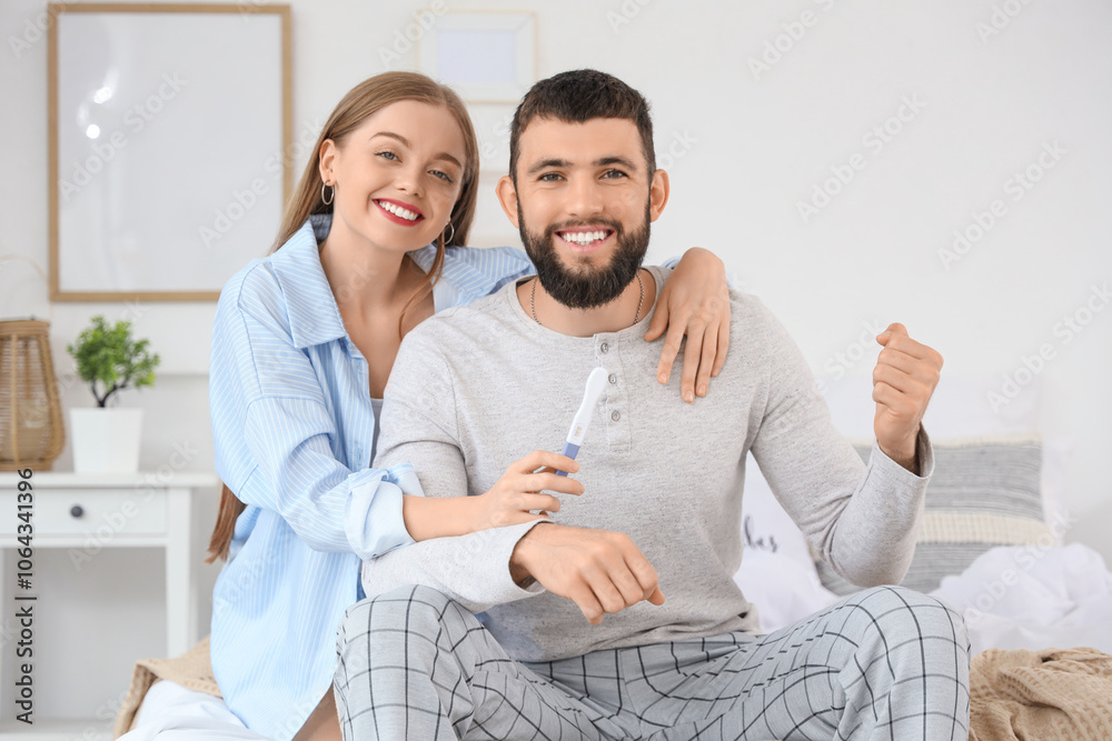 Happy young couple with pregnancy test hugging in bedroom