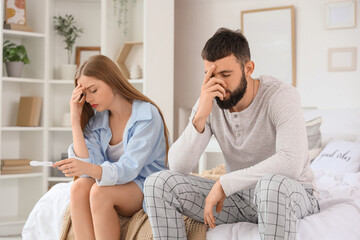 Wall Mural - Upset young couple with pregnancy test sitting in bedroom