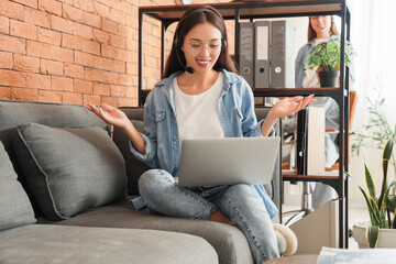 Wall Mural - Female Asian technical support agent working with laptop on sofa in office