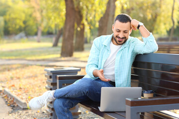 Canvas Print - Young man with laptop video chatting on bench in park