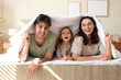 © Pixel-Shot - Little girl with her parents lying under soft blanket in bedroom
