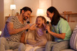 © Pixel-Shot - Happy family with microphones singing karaoke on sofa at home in evening