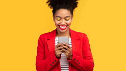 Poster - Gadget Addiction. Happy afro woman looking at mobile phone display isolated over orange studio wall, panorama