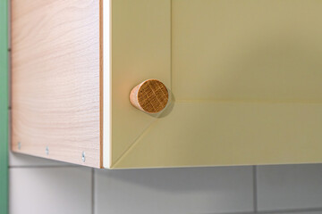 Wall Mural - Wooden handle attached to yellow sleek kitchen cabinet with a simple design. Solid oak cabinet knob close up view