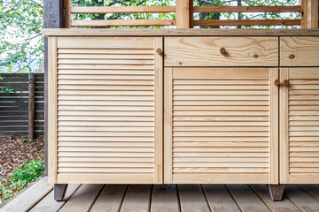 Wall Mural - Wooden cabinets of outdoor kitchen with louvered doors, drawers, wooden handles and plywood countertop, stand on a wooden terrace