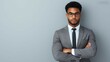 © lnwAI - Confident young businessman in a suit with glasses, standing with arms crossed against a gray background, symbolizing professionalism and success.