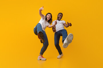 Wall Mural - Yo. Positive interracial couple fooling together, having fun and laughing at camera over yellow studio background, low angle view