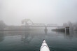 © Mint Images - View from a kayak of thick fog on Puget Sound, a bridge and dockside buildings.