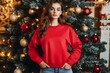 © PSCL RDL - Women red sweatshirt mockup with Christmas tree background. Young female model long sleeve tshirt mock up. Women's Gildan, basic pullover, winter casual jumper, front view, indoor lifestyle