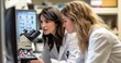 © thiquynh - Two women in lab coats are discussing data on a computer screen while working with a microscope