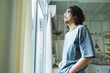 © eggeeggjiew - Portrait of Young Asian man with beard and eyeglasses looking thoughtfully out a window. Japanese male taking a deep breath air in a morning.