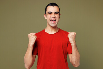 Young happy middle eastern man he wear red t-shirt casual clothes doing winner gesture celebrate clenching fists say yes isolated on plain pastel green background studio portrait. Lifestyle concept.