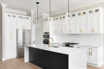 A kitchen with white cabinets and a black island, gold faucet and hardware, subway tile backsplash, and a waterfall marble countertop. No brands or labels.