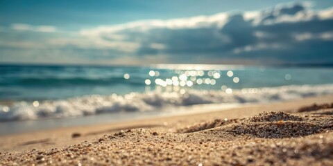 Close-up view of soft, golden sand on a beach with gentle waves and a blurred background of the ocean and sky, illuminated by the warm glow of the sun