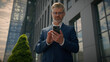 © Yuliia - Smiling old man middle aged businessman using mobile phone outdoors in city near office building smile at camera happy senior adult business male user employer holding smartphone broker real estate