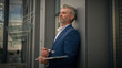 © Yuliia - Tired exhausted Caucasian old businessman elderly employer mature business man senior male middle-aged manager with laptop finish work city outdoors take off glasses leaning to wall of office building