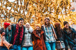 © charmedlightph - Smiling happy multi ethnic friends wearing winter clothes having fun on city street - Cheerful group of people celebrating eve day outside under Christmas tree decoration - Holidays life style concept