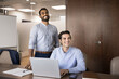 © fizkes - Cheerful multiethnic diverse male business friends posing for casual portrait at laptop, looking away, smiling, laughing, using laptop together, meeting in boardroom, presentation room