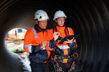 Female and male engineers work inside a large steel pipe. Workers build pipelines to transport oil, natural gas and fuels in industrial plants.