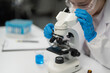 © Tj - Scientist adjusting microscope in lab with blue liquid, gloves, and face shield, focusing on research and investigation