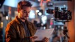 © VINA - A young man in a brown jacket reads a script on a film set with a camera in the background.