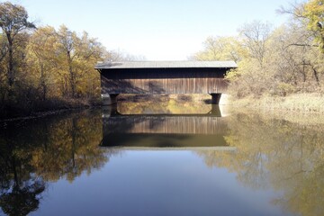 Wall Mural - Scenic Covered Bridge Surrounded by Vibrant Autumn Foliage Reflecting in Calm River