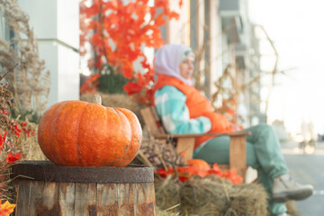 pumpkin lies on an old barrel, a woman sits on a bench in a hat and a green coat, decoration at a restaurant, autumn holidays, halloween, day of the dead, pumpkin savior, hay, leaves